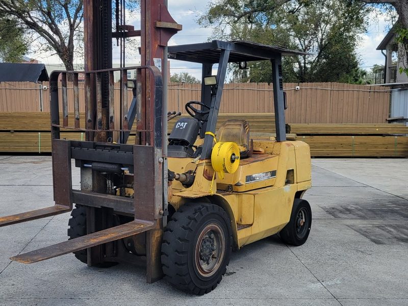 Yellow pneumatic tire forklift with a tall triple stage mast parked on a concrete lot
