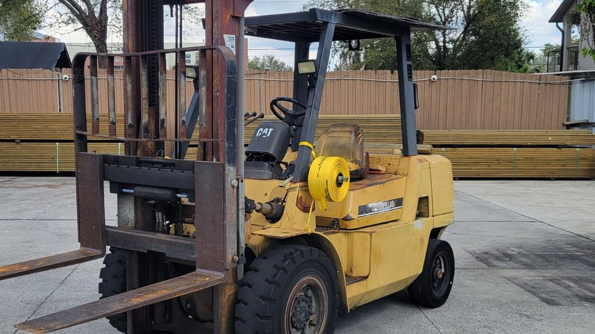 Yellow pneumatic tire forklift with a tall triple stage mast parked on a concrete lot