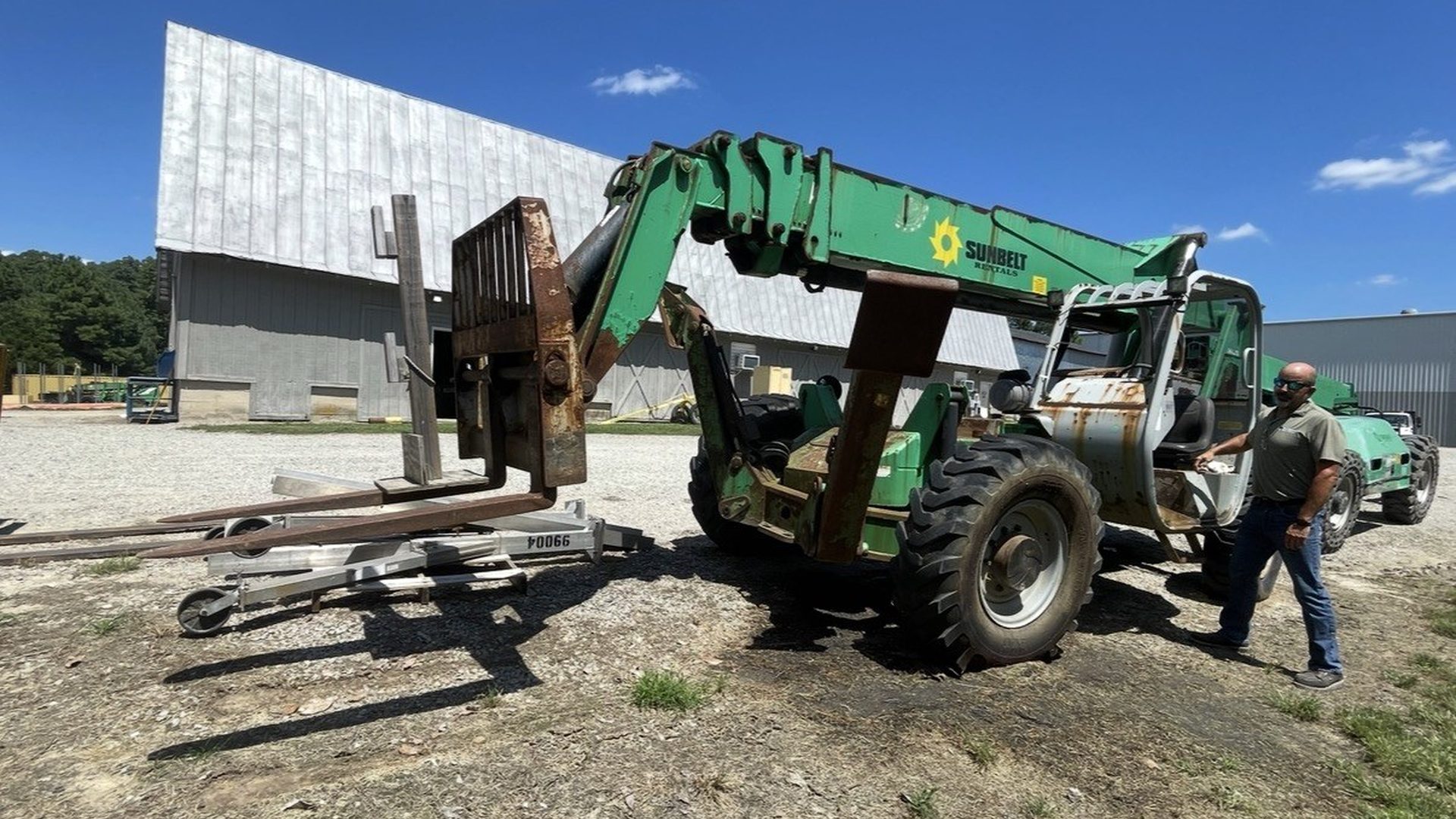Green telehandler forklift with loose forks and attachments laid out on the ground before removal