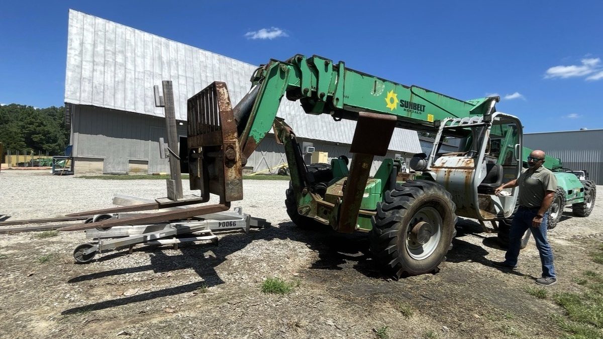 Green telehandler forklift with loose forks and attachments laid out on the ground before removal